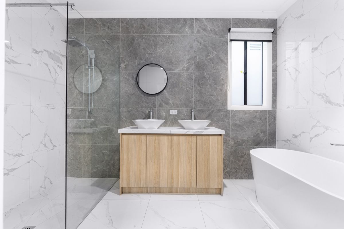 Baño reformado con azulejos blancos, lavabo con espejo y ducha de cristal